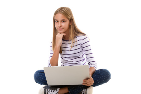 Pretty young teen girl sitting on the floor with crossed legs and using laptop isolated over white backgroundの写真素材