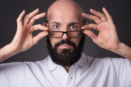 Portrait of bald unshaven man holding glasses on dark backgroundの写真素材