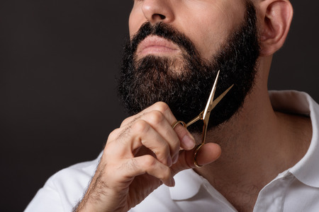 Cropped image of bearded man with scissord over dark backgroundの写真素材