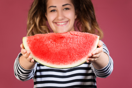 Funny portrait happy smiling young girl holding slice of watermelon over colorful pink background.Main focus on the watermelonの写真素材