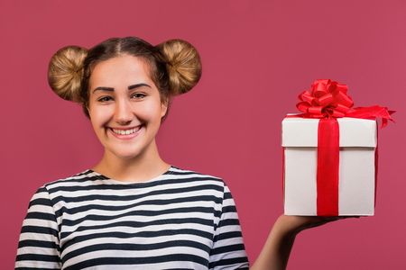 Picture of hipster girl with funny hairstyle holding the gift box on hand palm isolated over pink backgroundの写真素材