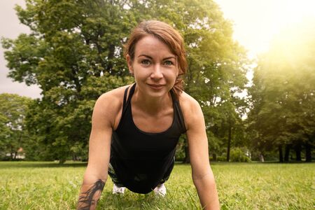 Push ups or press ups exercise by young woman, working out on grass in parkの写真素材