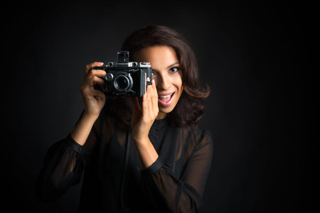 Beautiful brunette woman taking a photo by  vintage camera with happy face  on dark background