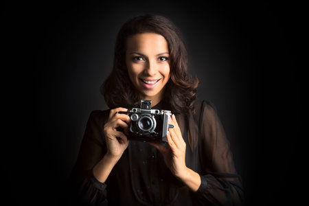 Portrait of Beautiful smiling brunette woman holding  vintage camera on dark background