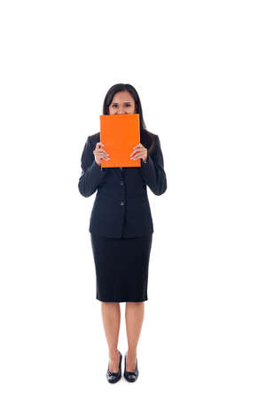 Smiling asian modern business woman holding book and hidden behind the book, looking at camera, full length portrait isolated on white backgroundの写真素材