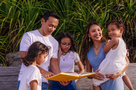 family, leisure and people concept-big asian happy family with three daughters reading the book, enjoying summer vacation together.の写真素材