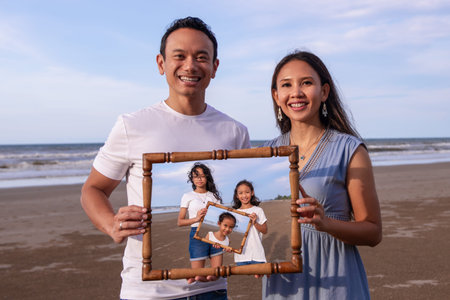 family, leisure and people concept-asian happy parents holding picture of frame of children on the...