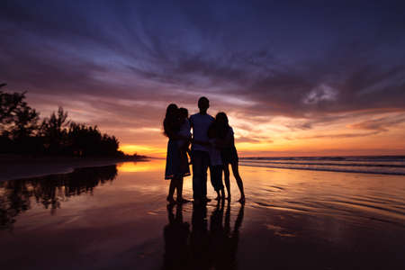 Silhouettes of happy family on beach during sunsetの写真素材