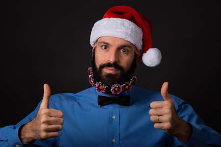 Christmas, holidays, barbershop and style concept - handsome bearded santa claus man with small flowers in long beard showing ok sign with both handsの写真素材