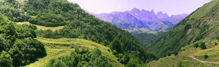 A majestic panorama of a rocky mountain range with forest-covered slopes of mountains in the foreground. A country road stretching into the distanceの写真素材