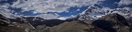 Clouds in the blue sky hit the top of the magnificent Kazbek. Mountain landscape panorama.