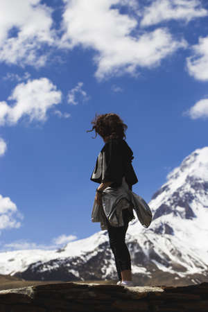 Woman traveler enjoys the view of snow-capped mountain peaks. Hiking in the mountains, active lifestyle for girlの写真素材