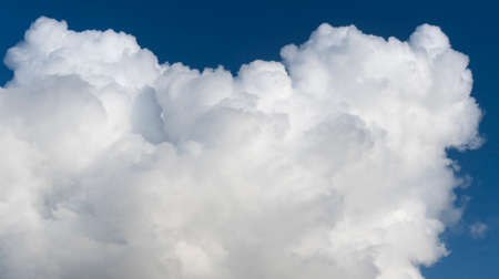 White fluffy cumulus cloud on a bright blue sky in sunny weather. Beautiful background, screen saverの写真素材