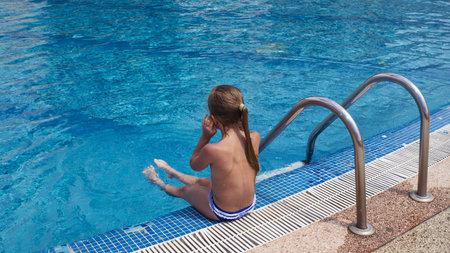 The girl sits on the side of the pool. Healthy lifestyle. Child on vacation at the resort.