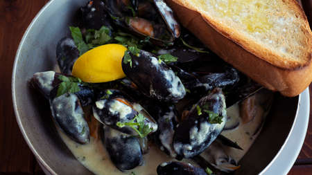 Delicious mussels in a creamy sauce in a pan close-up. White toasted bread with garlicの写真素材