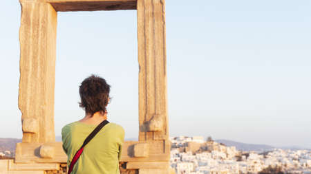 A tourist photographs a Greek city on an island through ancient ruins. White houses on the hill.の写真素材