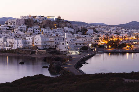 Pink morning over a mountainous Greek island with a white city. Street lights are reflected in the calm seaの写真素材