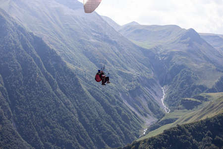 Paragliding with a pair of instructors. Bright blue sky with beautiful white fluffy clouds. Leisure with active adventures. Mountains landscape panoramaの写真素材