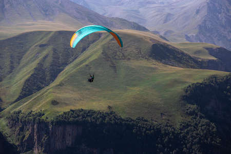 A man on a paraglider takes a selfie. Mountain gorge with green slopes, a parachute with people flies over the cliff. Beautiful view panorama landscapeの写真素材