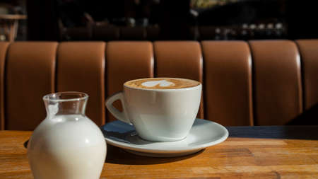 A cup of aromatic coffee on a wooden table in a cafe. Morning sun illuminated breakfast. daily routine. Beautifully decorated cappuccino foamの写真素材