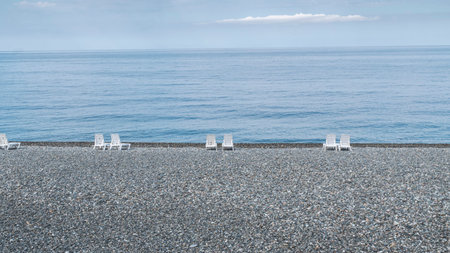 Empty pebble beach with white sun loungers on a sunny day. Seascape in good weather. Lack of people at the resortの写真素材