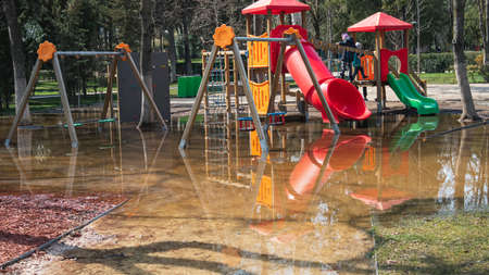 Children's playground in a public park in the city. The swing and pipes are in a puddle. Impossible to playの写真素材