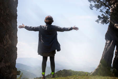 A young woman stands on top of a mountain with her arms outstretched in the wind in the sun. The concept of freedom and purification.の写真素材