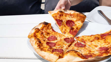 The child takes a piece of pizza from the dish. Bright tasty pepperoni close-upの写真素材