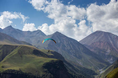 A man on a paraglider takes a selfie. Mountain gorge with green slopes, a parachute with people flies over the cliff. Beautiful view panorama landscapeの写真素材