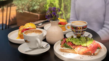 Beautifully decorated toast with salmon and avocado, egg benedict and cappuccino Breakfast is the go-to time for meetingsの写真素材