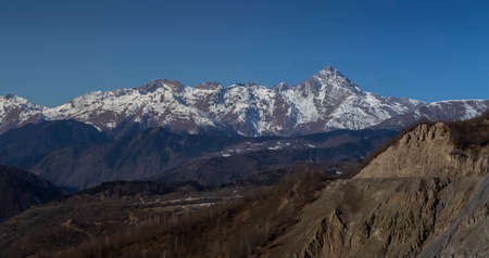 Panorama of the mountain range. The peaks are covered with snow. Dangerous road on a mountain slopeの写真素材