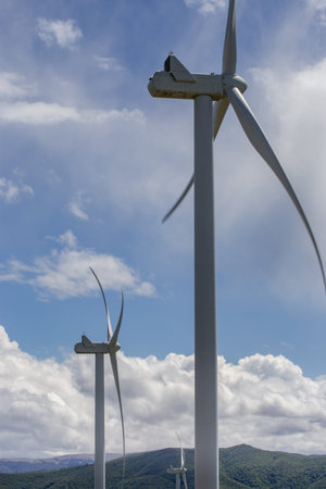 Windmills in the mountains. Mountain range with green grass, white fluffy clouds on the blue sky.