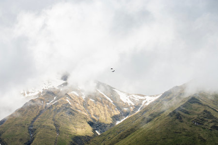 A breathtaking view of misty mountains in Georgia, their snow-capped peaks partially hidden by...