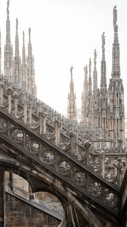 The image shows the intricate Gothic architecture of Milan's iconic Duomo Cathedral. Tall spires, ornate carvings, detailed statues, and decorative stonework adorn the structure, showcasing its grandeur and artistry.の写真素材