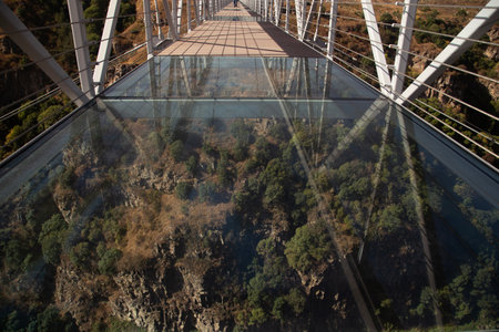 A glass suspension bridge in Georgia, offering a thrilling view of a deep canyon below. Transparent panels reveal the rocky gorge and green trees, creating a breathtaking mix of nature and engineering.の写真素材