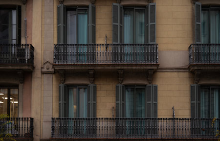Traditional building facade in Barcelona, featuring ornate iron balconies, symmetrical windows with shutters, stone architecture, muted beige tones, urban elegance, historic charm, and Mediterranean style.の写真素材