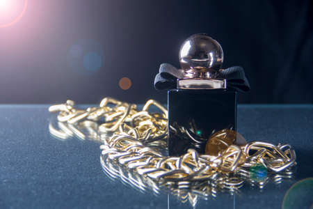 A black bottle of womens perfume on a dark background. Decoration in the form of a gold chain. A bottle of fragrant perfume on a dark background. Womens perfume.の写真素材