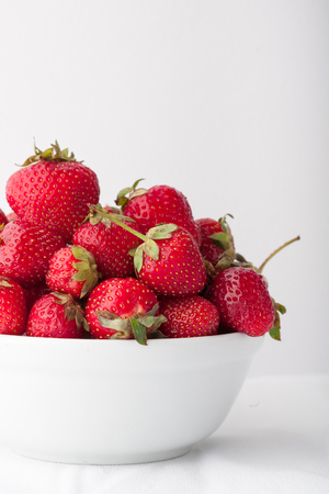 Strawberries in a white bowl on a white background. Copy space. Vertical image.の写真素材