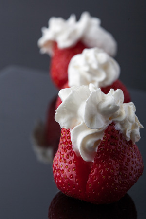 Three strawberries with whip cream on a glossy black background. Vertical image. Copy spaceの写真素材