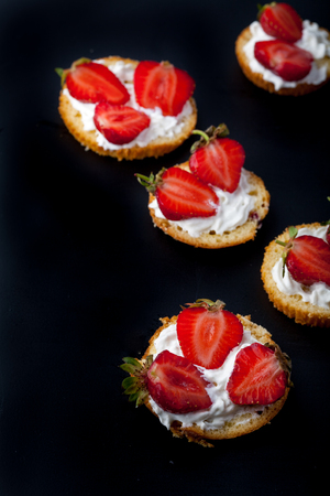 Fluffy buttermilk biscuits shortcake with red ripe strawberries and fresh whipped cream on a black background. Vertical image. Copy spaceの写真素材