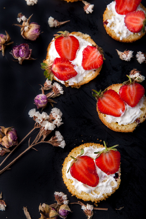 Fluffy buttermilk biscuits shortcake with red ripe strawberries and fresh whipped cream on a black background with flowersの写真素材