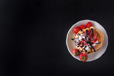 Homemade pancakes with strawberries, whipped cream and chocolate topping, decorated on black background. Overhead shot. Flat lay. Copy space. Vertical imageの写真素材