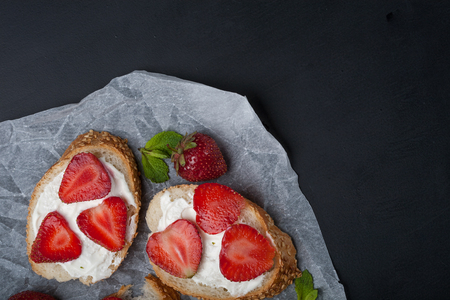 Toasts or bruschetta with strawberries on cream cheese on black background. Top view. Copy spaceの写真素材