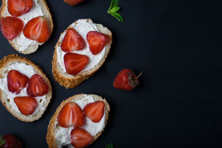 Toasts or bruschetta with strawberries on cream cheese on black background. Top view. Copy spaceの写真素材