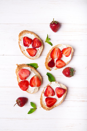Toasts or bruschetta with strawberries on cream cheese on black background. Top view. Copy spaceの写真素材