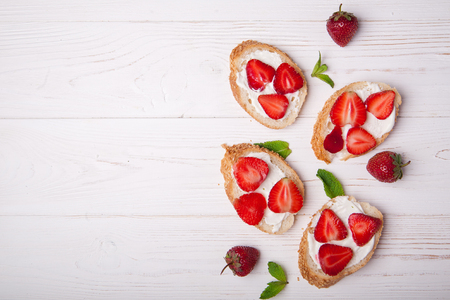 Toasts or bruschetta with strawberries on cream cheese on white background. Top view. Copy spaceの写真素材