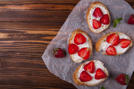 Toasts or bruschetta with strawberries on cream cheese on wooden background. Top view. Copy spaceの写真素材