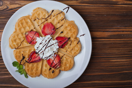 Norwegian heart shaped waffles topped with strawberries,  mint and whipped cream on white plate and wooden background. St. Valentine's Day breakfast. Romantic breakfast. Copy spaceの写真素材