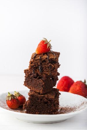 Stack of brownies decorated with strawberries on white plate on white background. Copy space.の写真素材