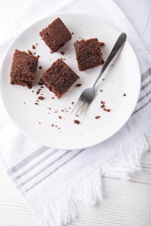Brownie slice on a white plate on white napkin on white wooden background. Copy space. Flat lay. Overheadの写真素材